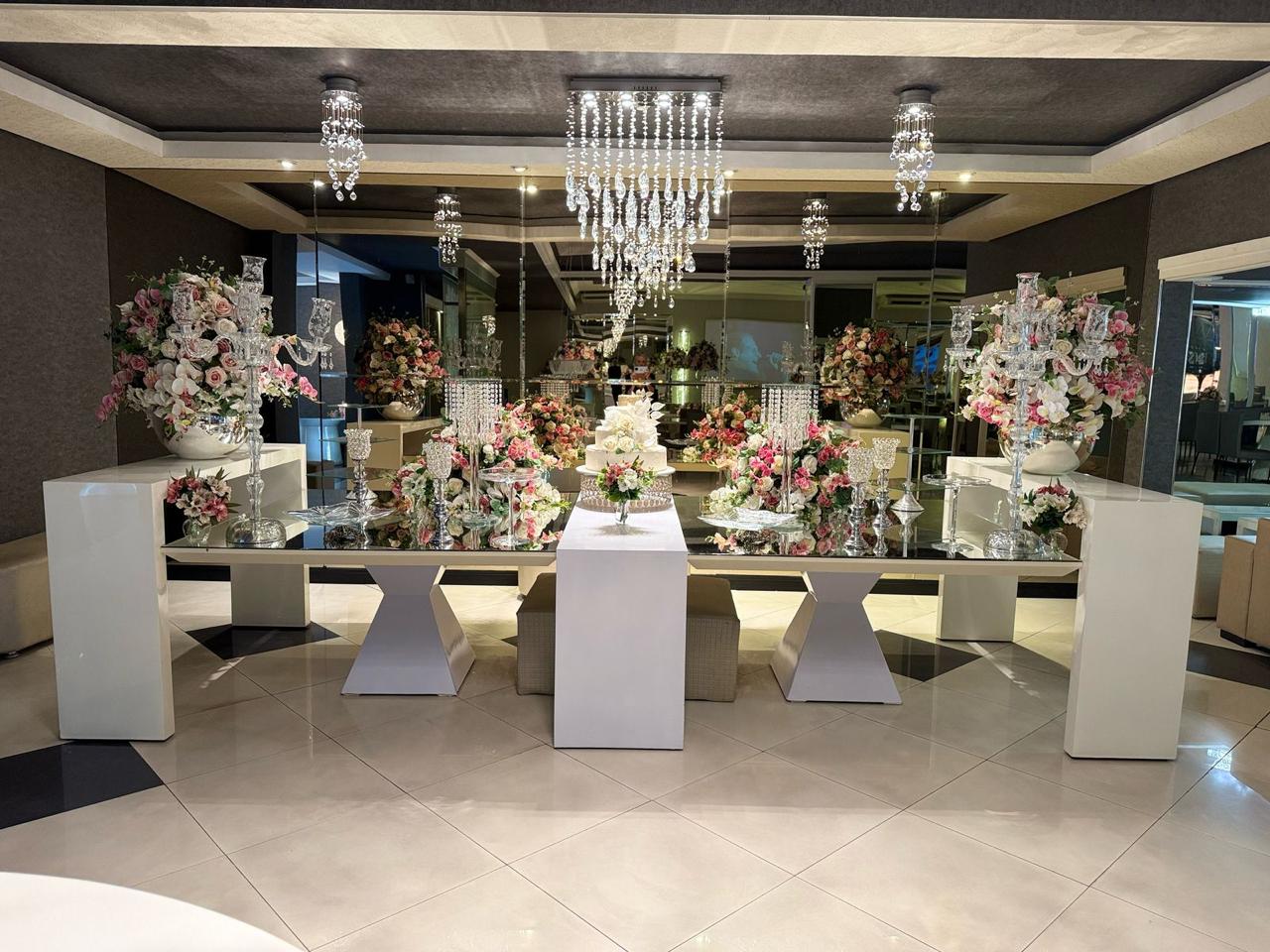 Mesa do bolo do Salão Perrie com bancadas espelhadas, castiçais de cristal e lustres suspensos