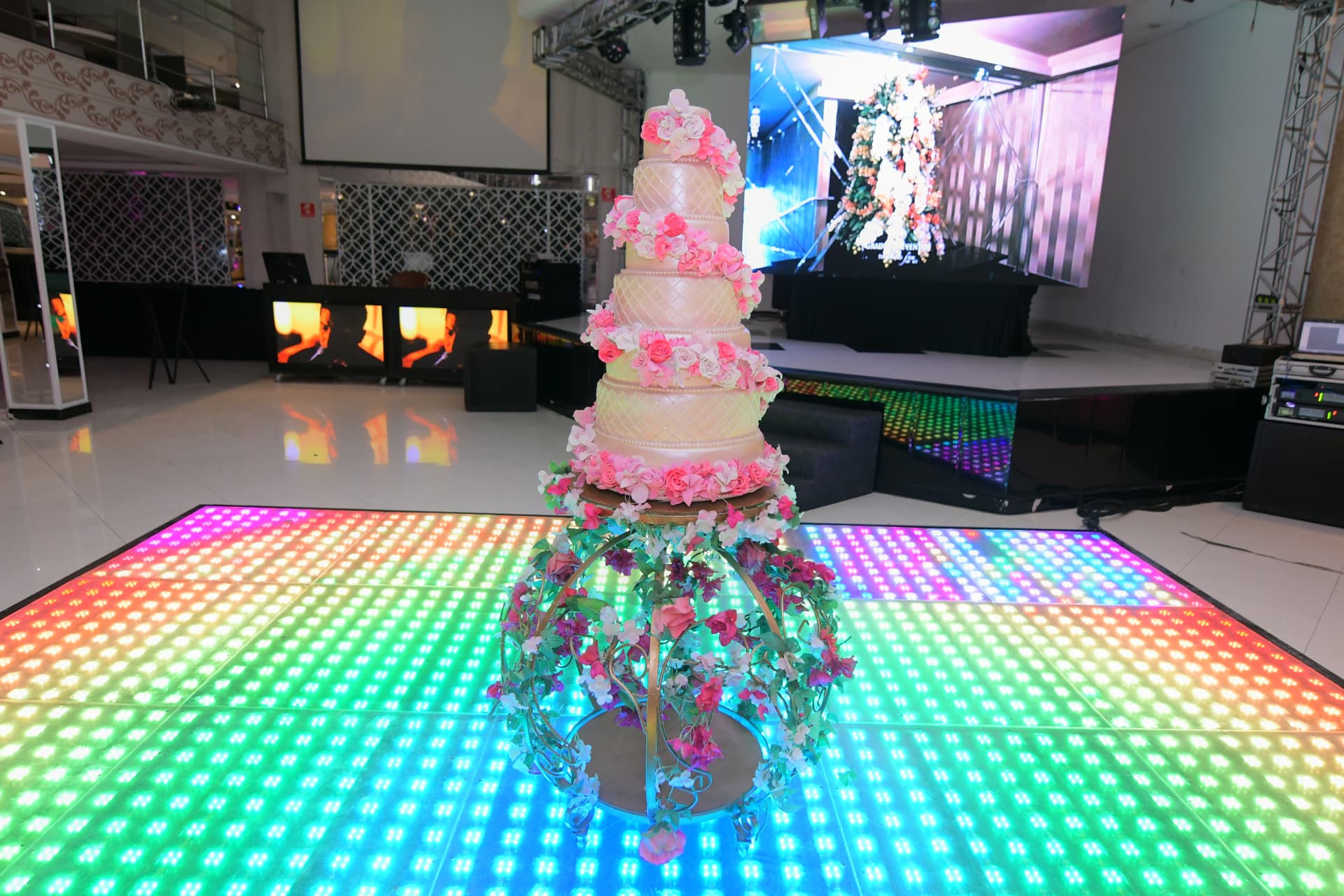 Bolo de casamento de andares floridos no centro da pista em LED do San Pelegrine, com telão e palco ao fundo
