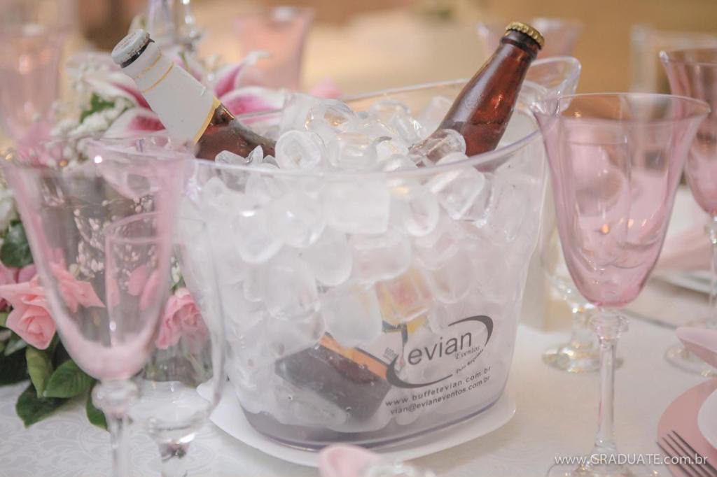 Balde de gelo personalizado Evian com bebidas geladas entre taças de cristal rosé e arranjo de lírios