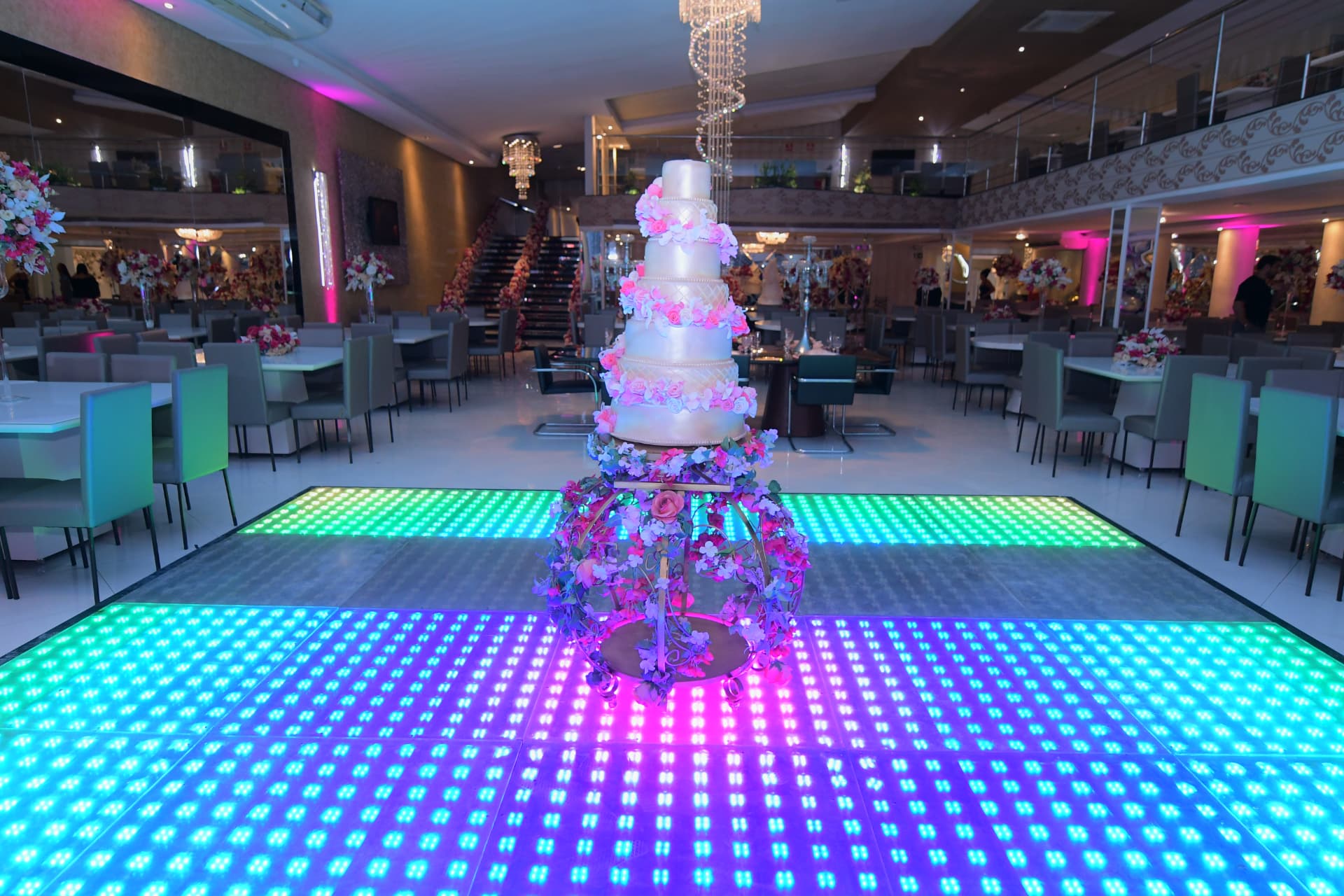 Pista de dança em LED do San Pelegrine com bolo suspenso sob lustre de cristal e mesas ao redor