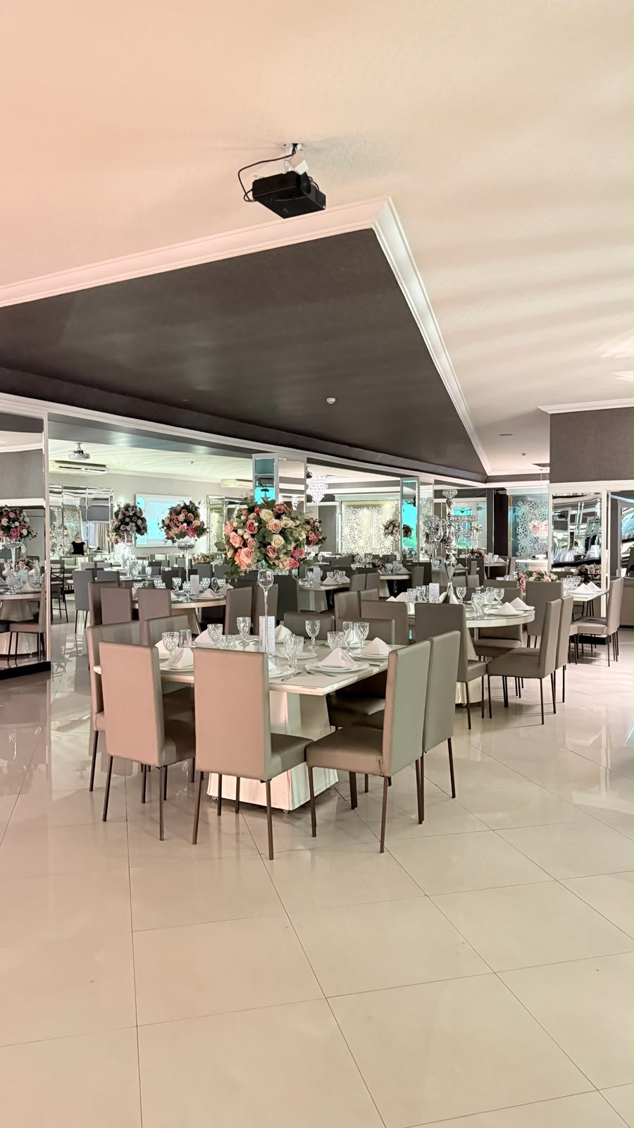 Mesas do Salão Perrie com colunas espelhadas, arranjos de rosas e piso porcelanato reflexivo