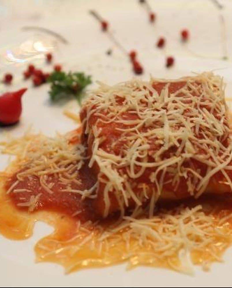 Prato empratado com massa ao sugo coberta de queijo em lascas e pimenta rosa sobre louça branca